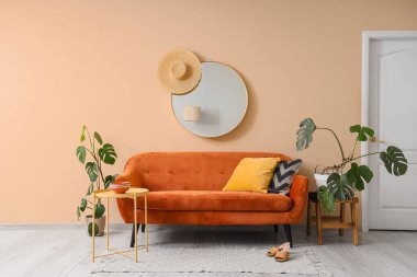 Rahat kahverengi kanepe, ev bitkileri ve odanın iç tarafındaki bej duvarın yanındaki masalar.