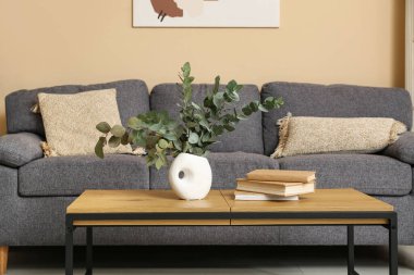 Oturma odasının iç tarafındaki masada okaliptüs dalları olan kitap ve vazo.