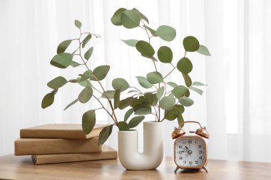 Oturma odasındaki masada okaliptüs dalları olan çalar saat ve vazo, yakın plan.