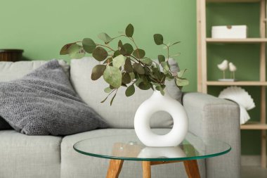 Oturma odasındaki masada okaliptüs dalları olan vazo, yakın plan.