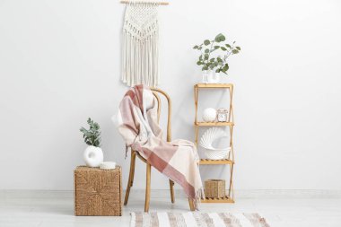 Sandalyesi, raf ünitesi ve sepette okaliptüs dalları olan şık bir oda.