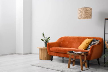 Rahat kanepesi ve beyaz duvarın yanındaki masaları olan modern bir oturma odası.