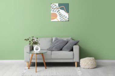 Oturma odasının içinde okaliptüs dalları olan kanepe, puf, masa ve vazo.