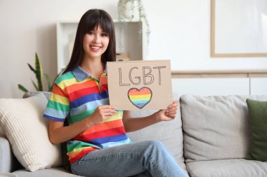 Kelime LGBT ile pankart tutan ve oturma odasında kanepede oturan güzel genç bir kadın.