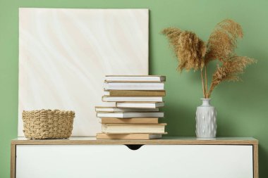 Yığınla kitap, hasır sepet ve yeşil duvarın yanındaki dolapta otlar, yakın plan.