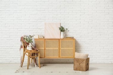 Oturma odasının iç tarafındaki beyaz tuğla duvarın yanında okaliptüs dalları olan çekmeceler ve vazolar.