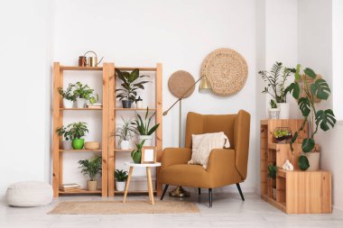 Oturma odasının iç tarafındaki beyaz duvarın yanındaki raflar, masa, puf, koltuk ve bitkiler.