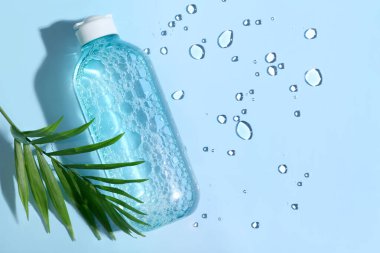 Mavi arka planda bir şişe mikiler suyu ve tropikal yaprak, yakın plan.