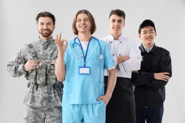 Aydınlık arkaplanda farklı mesleklerden üniformalı bir grup genç adam.