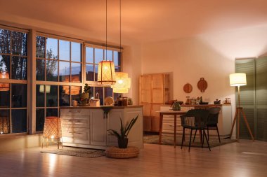 Akşamları tezgahları, yemek masası ve parlayan lambaları olan modern mutfak.