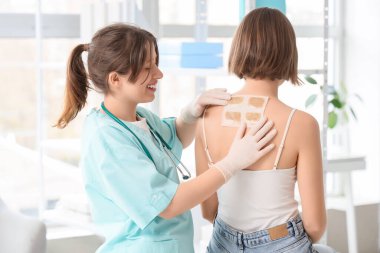 Kadın doktor klinikte hastanın sırtına hardal yapıştırıyor.