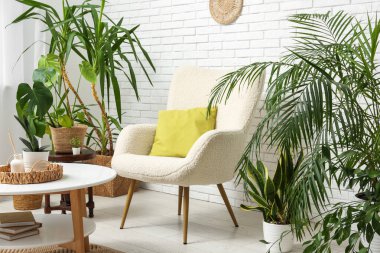 Beyaz tuğla duvarın yanında koltuk, masa ve çiçeklerle dolu bir oda.