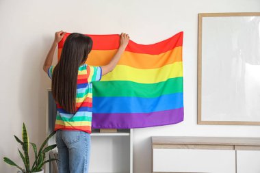Oturma odasındaki duvara LGBT bayrağı asan genç bir kadın.