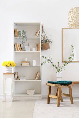 Kitap rafı, nergisleri ve çiçek açan vazolarla aydınlık oturma odasının içinde.