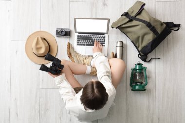 Hafif ahşap zeminde aksesuarlı dizüstü bilgisayar kullanan kadın gezgin.