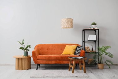 Rahat kanepesi ve beyaz duvarın yanındaki masaları olan modern bir oturma odası.