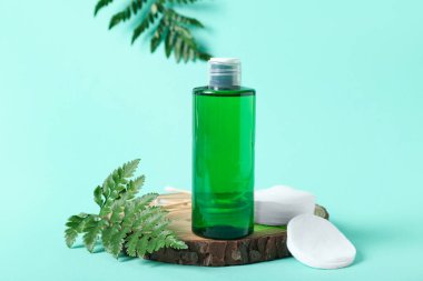 Bir şişe mikiler suyu, pamuk pedler ve turkuaz arka planda ahşap bir dilim, yakın plan.