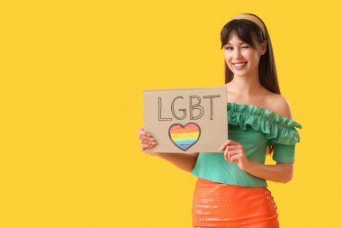 Sarı arka planda LGBT yazan bir pankart tutan güzel bir genç kadın.