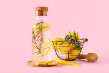 Biberiyeli bir şişe taze limonata ve pembe arka planda limonlar.
