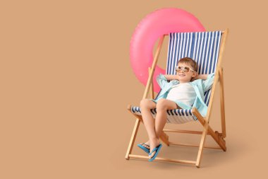 Kahverengi arka planda şezlongda oturan şişme yüzüklü şirin küçük çocuk. Seyahat kavramı