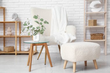 Koltuk, masa, pouf ve vazo, oturma odasının içinde okaliptüs dalları, yakın plan.