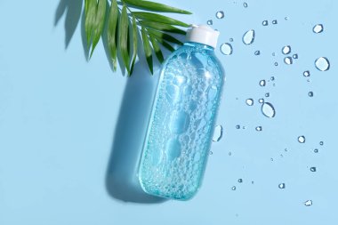 Mavi arka planda bir şişe mikiler suyu ve tropikal yaprak, yakın plan.