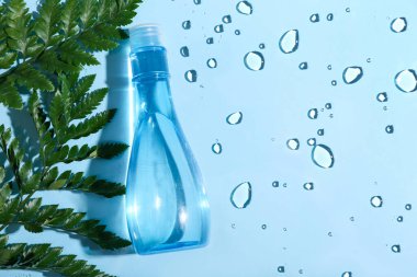 Bir şişe mikiler suyu ve mavi arka planda yeşil yapraklar, yakın plan.