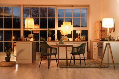 Akşamları tezgahları, yemek masası ve parlayan lambaları olan modern mutfak.