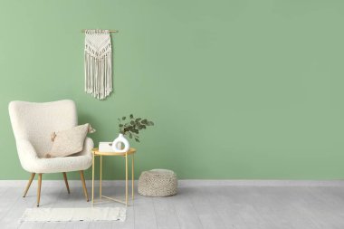 Koltuk, puf, masa ve vazo, oturma odasının içinde okaliptüs dalları var.