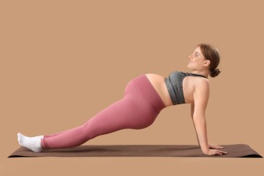 Kahverengi arka planda yoga minderinde antrenman yapan genç ve sportif bir kadın.