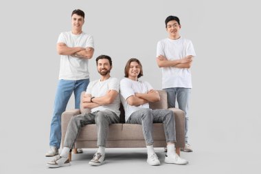 Beyaz tişörtlü ve arka planda kanepesi olan bir grup genç adam.