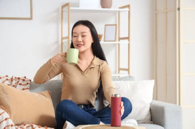 Asyalı kadın evde termostan sıcak çay içiyor.