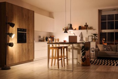 Geceleri tezgahları, masa lambaları ve parlayan lambaları olan modern mutfağın içi.