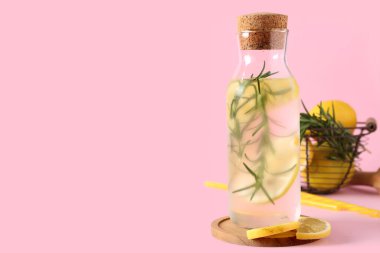 Biberiyeli bir şişe taze limonata ve pembe arka planda limonlar.