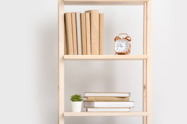 Beyaz duvarın yanında kitap ve dekor yığını olan raf ünitesi