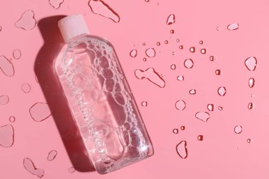 Pembe arka planda bir şişe mikiler suyu ve su damlası, yakın plan.