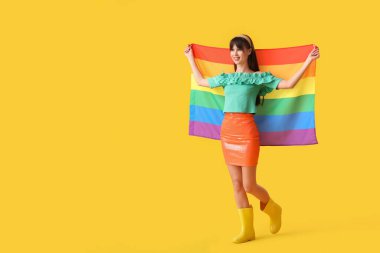 Sarı arka planda LGBT bayrağı olan güzel genç bir kadın.