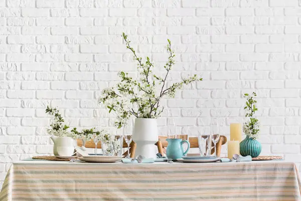 Tabakları, bardakları ve çiçek açan ağaç dalları olan zarif bir masa.