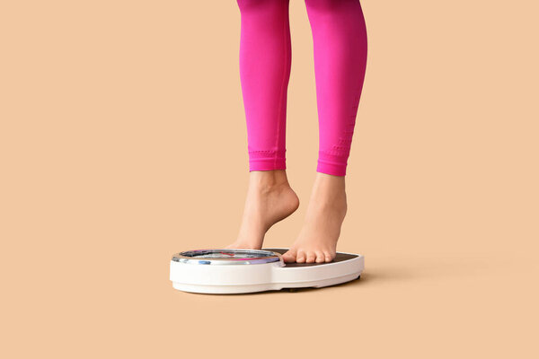 Legs of sporty woman measuring her weight on scales against beige background