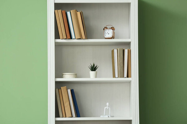 Shelving unit with books and decor near green wall