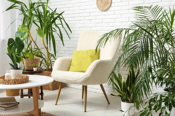 Beyaz tuğla duvarın yanında koltuk, masa ve çiçeklerle dolu bir oda.