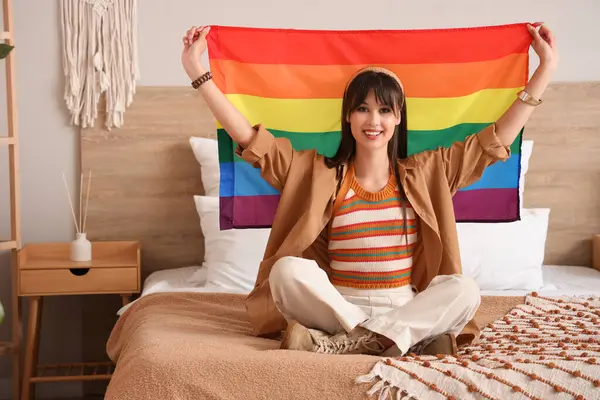 Yatak odasında LGBT bayrağıyla oturan güzel genç bir kadın.