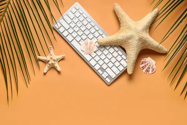 Palmiye yaprakları, kabukları ve turuncu arka planda deniz yıldızları olan bilgisayar klavyesi