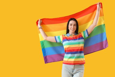 Sarı arka planda LGBT bayrağı olan gökkuşağı tişörtlü güzel bir kadın.