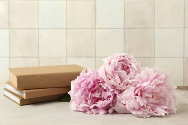 Üzerinde güzel şakayık çiçekleri ve kitaplar olan vazo bej fayans duvarın yanında, yakın plan.