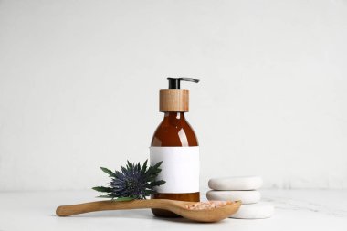 Deniz tuzu, kozmetik ürün şişesi ve hafif arka planda spa taşlarıyla kaşık.