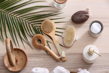 Farklı banyo malzemeleri, kozmetik ürünler ve ahşap arka planda palmiye yaprağı.