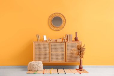 Çekmece sandığı, vazo, otlu vazo ve odanın içindeki sarı duvarın yanındaki ayna.