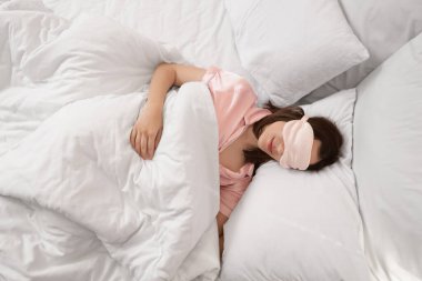 Maskeli genç bir kadın yatak odasında yastıklarda uyuyor.