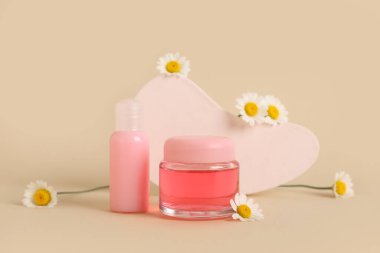 Plaster standı, şişe ve kozmetik ürünler kavanozu bej arka planda papatya çiçekleri, yakın plan